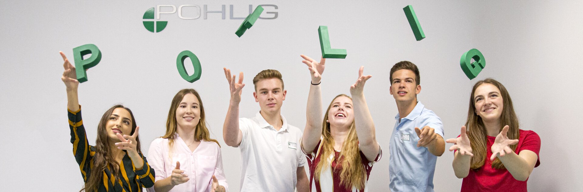 Auszubildende stehen hinter einem Tresen und Werfen die Buchstaben "Pohlig" in die luft. | © Pohlig GmbH