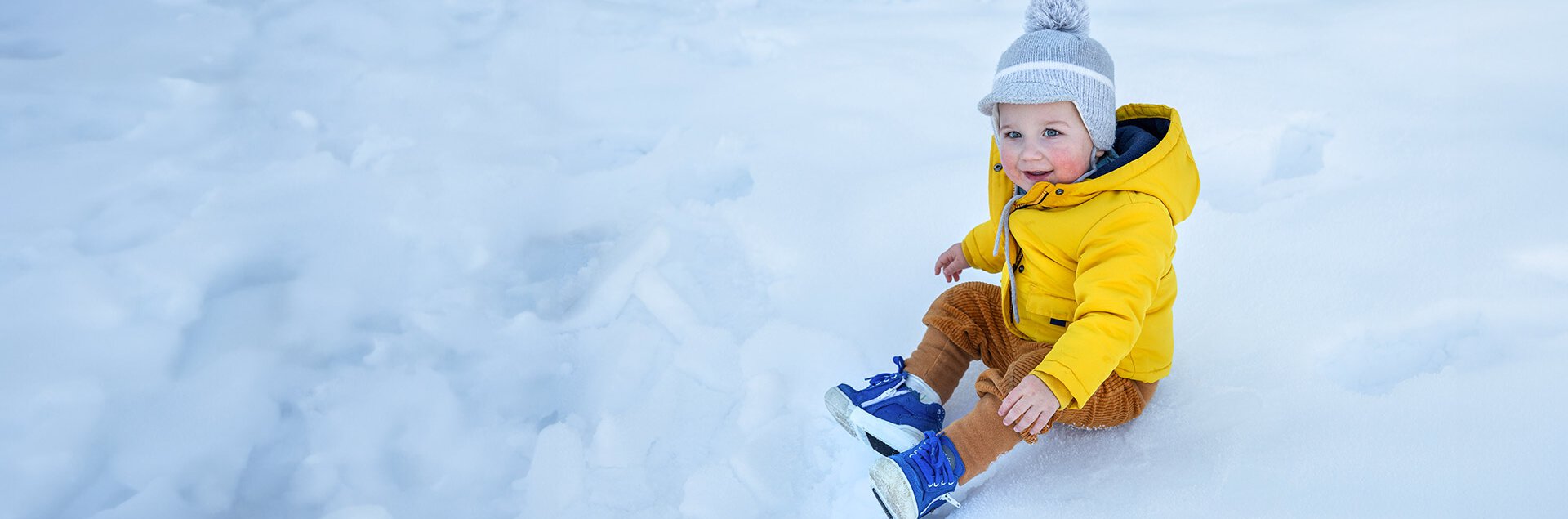 Ein kleiner Junge sitzt draußen im Schnee, probiert seine neuen Winterorthesenschuhe aus und lächelt in die Kamera. | © Pohlig GmbH