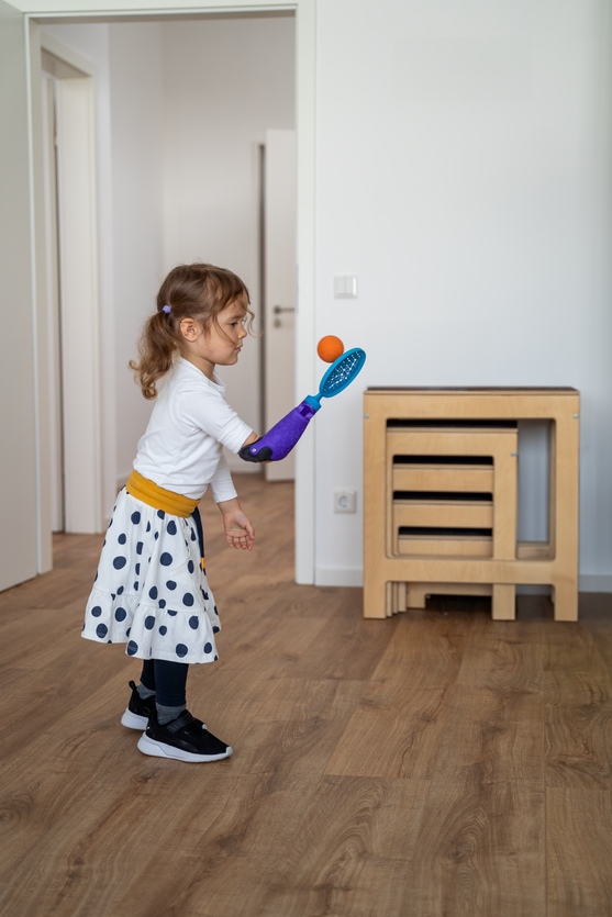 Mädchen spielt mit Ball und trägt dabei den Tennisschlägeraufsatz auf ihrer FIRST Prothese