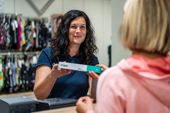 Sanitätshaus Mitarbeiter reicht Kompressionsstrumpf über Theke | © Pohlig GmbH